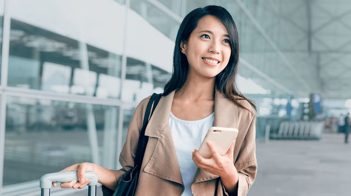 Woman smiling with suitcase and smartphone in airport terminal.