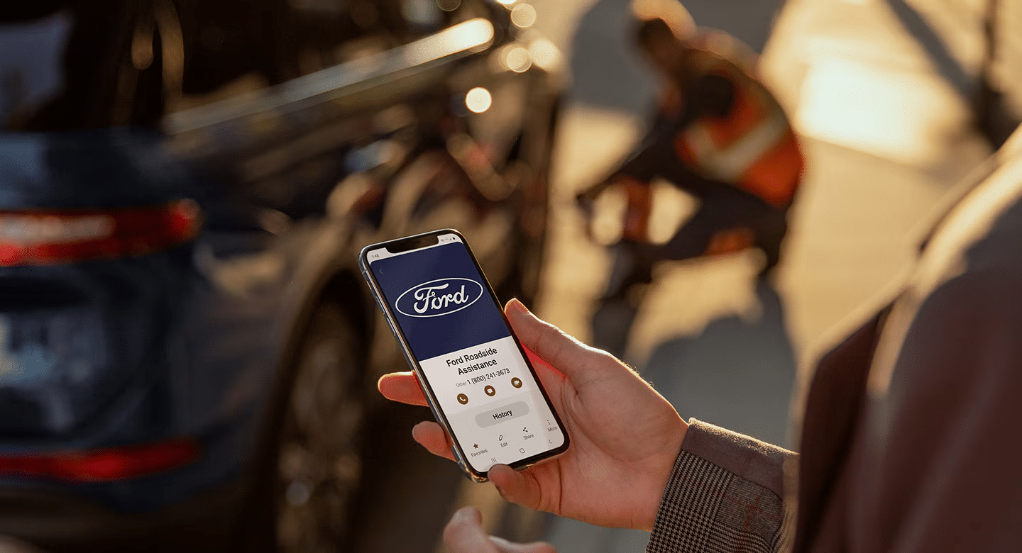 Person using Ford Roadside Assistance app on smartphone near parked car.