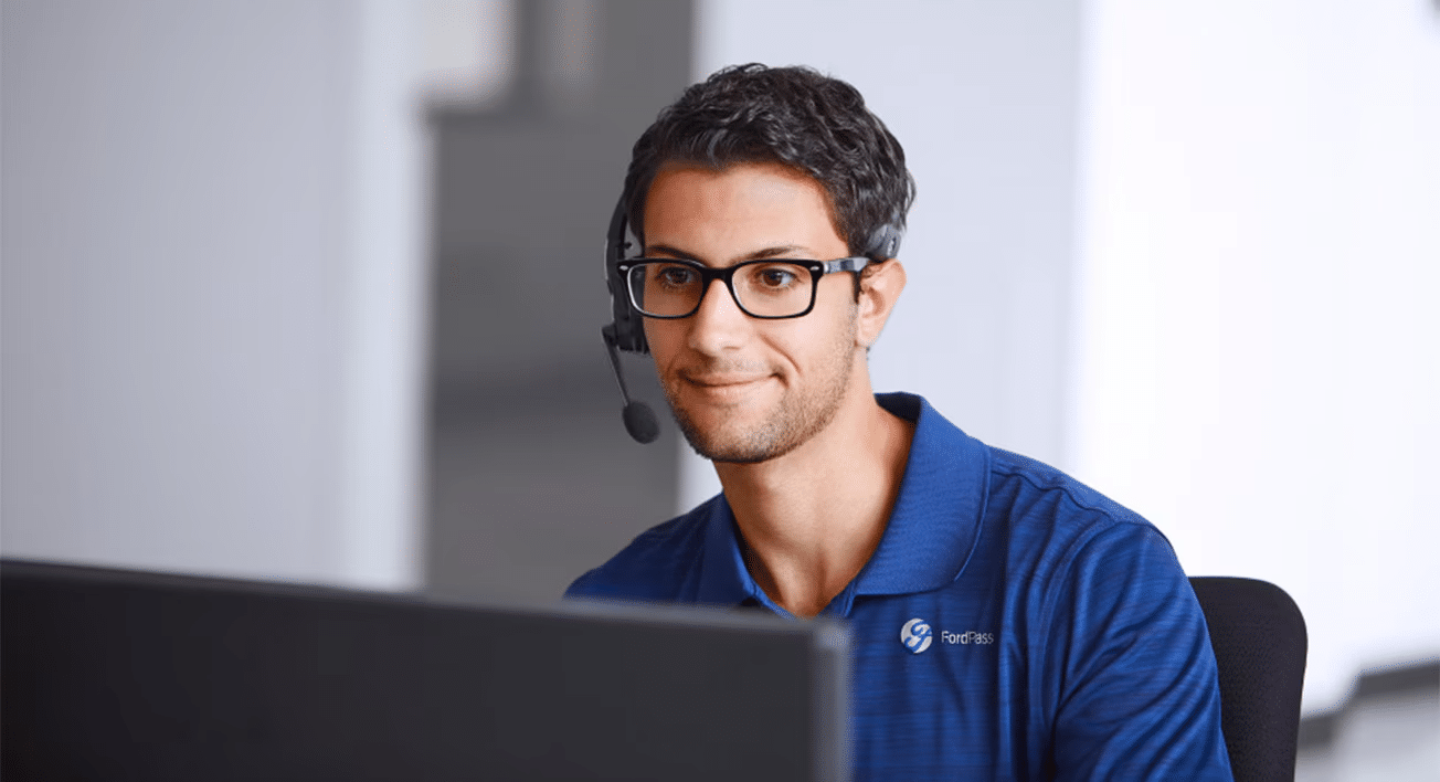 Customer service representative with glasses and headset, wearing a FordPass polo, looking at a computer.