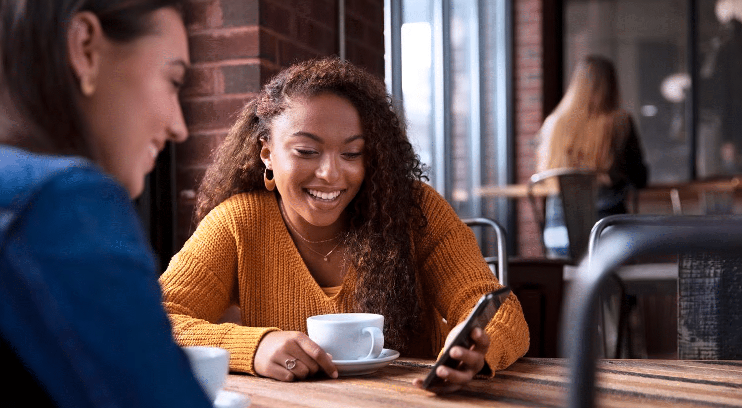 Two friends enjoying coffee at a café, smiling and looking at a phone.