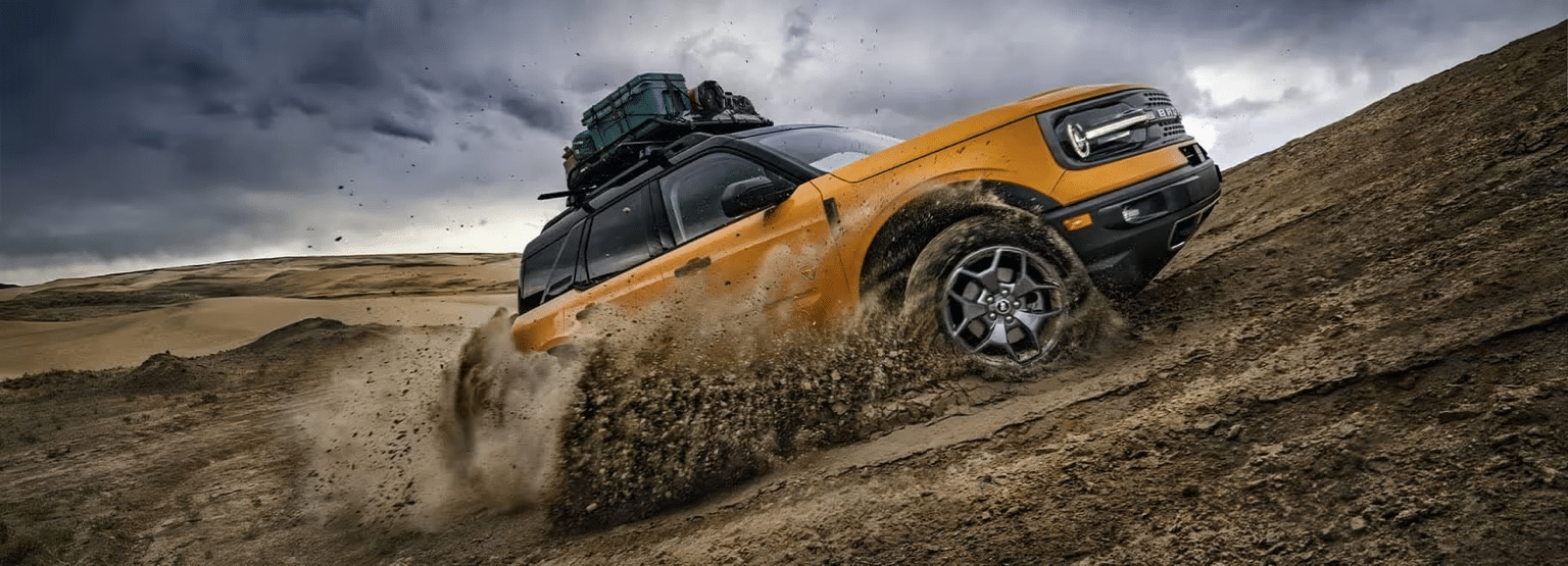 Orange SUV with roof cargo climbs muddy hill under stormy sky, showcasing off-road capability.