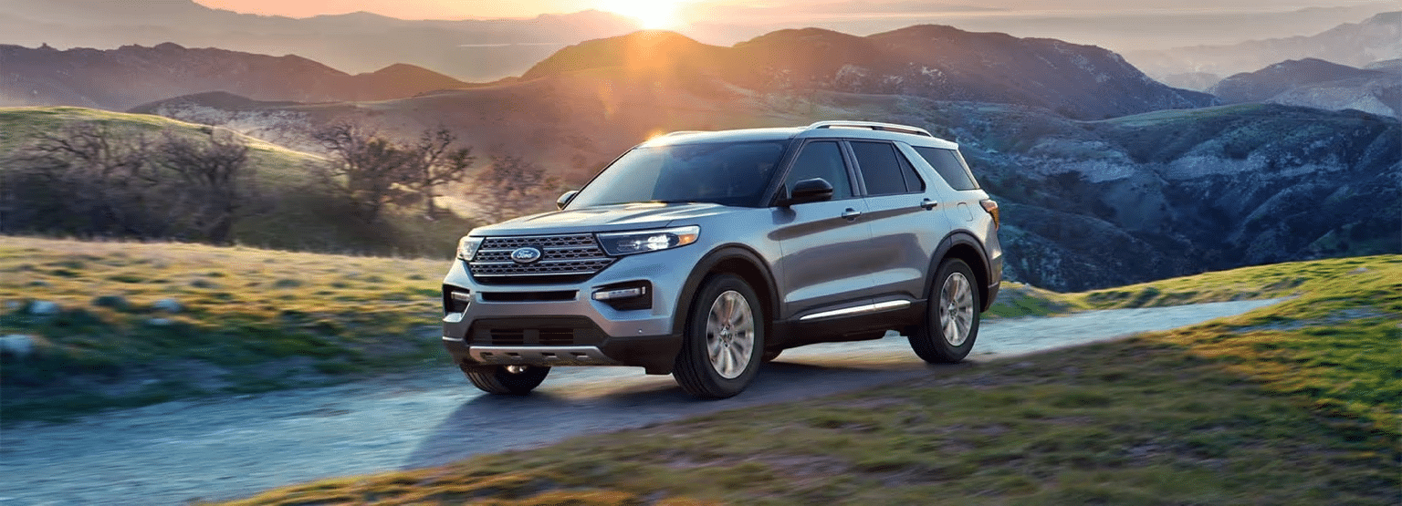 SUV driving on a scenic mountain road at sunset, showcasing rugged landscape and vibrant sky.