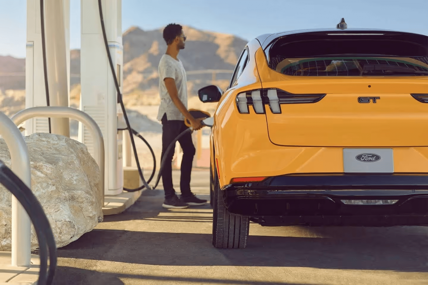 Man charging a Ford GT in a sunny desert setting, highlighting electric vehicle convenience.