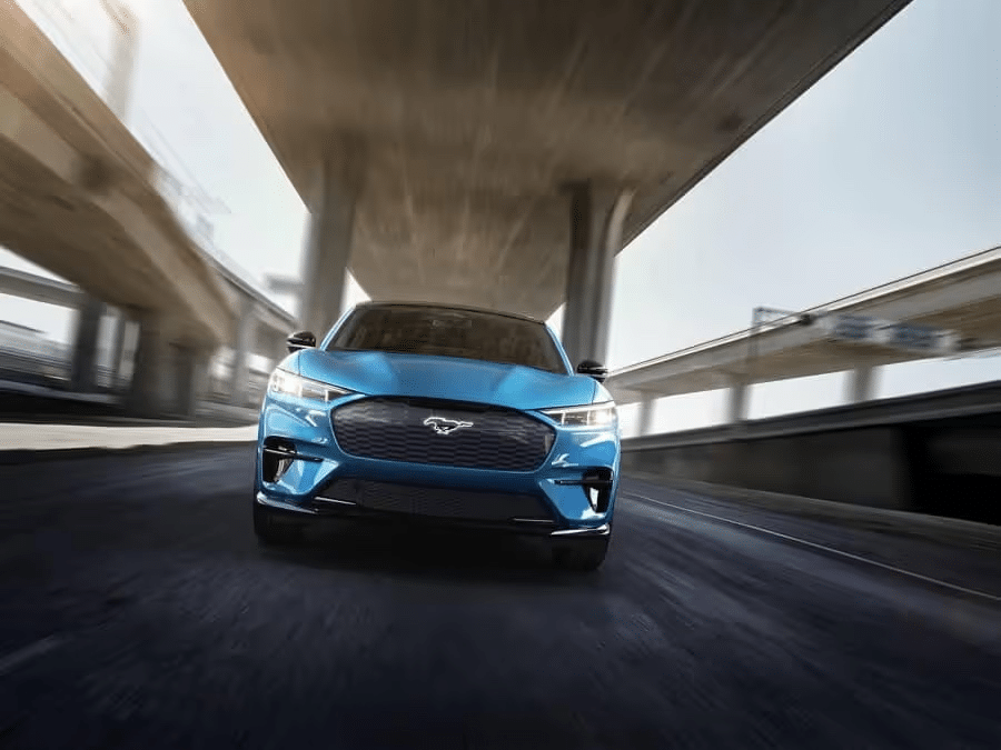 Blue sports car driving under a highway overpass, capturing a dynamic front view.