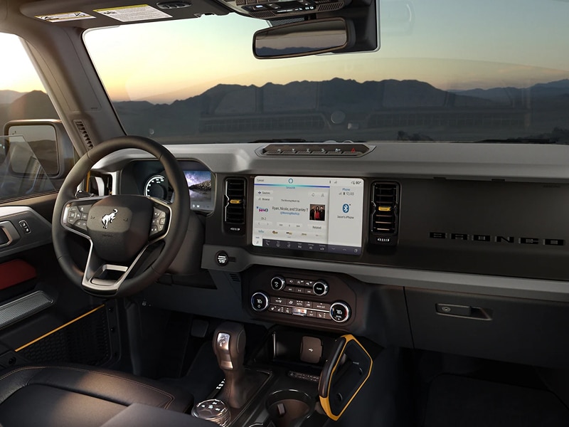 Interior of a modern SUV with a steering wheel, dashboard, and touchscreen display at sunset.