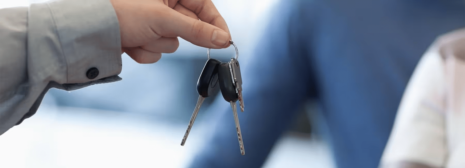 Hand holding car keys, symbolizing vehicle ownership or rental. Blurred background.