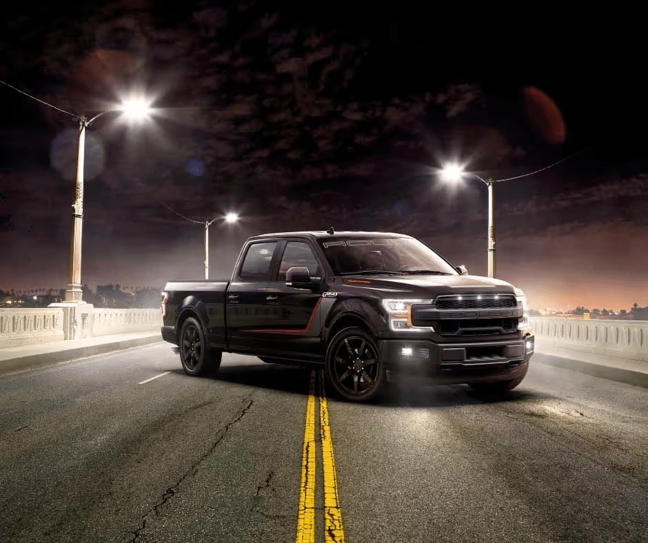 Black pickup truck parked on a lit bridge at night, silhouetted against a dark cloudy sky.