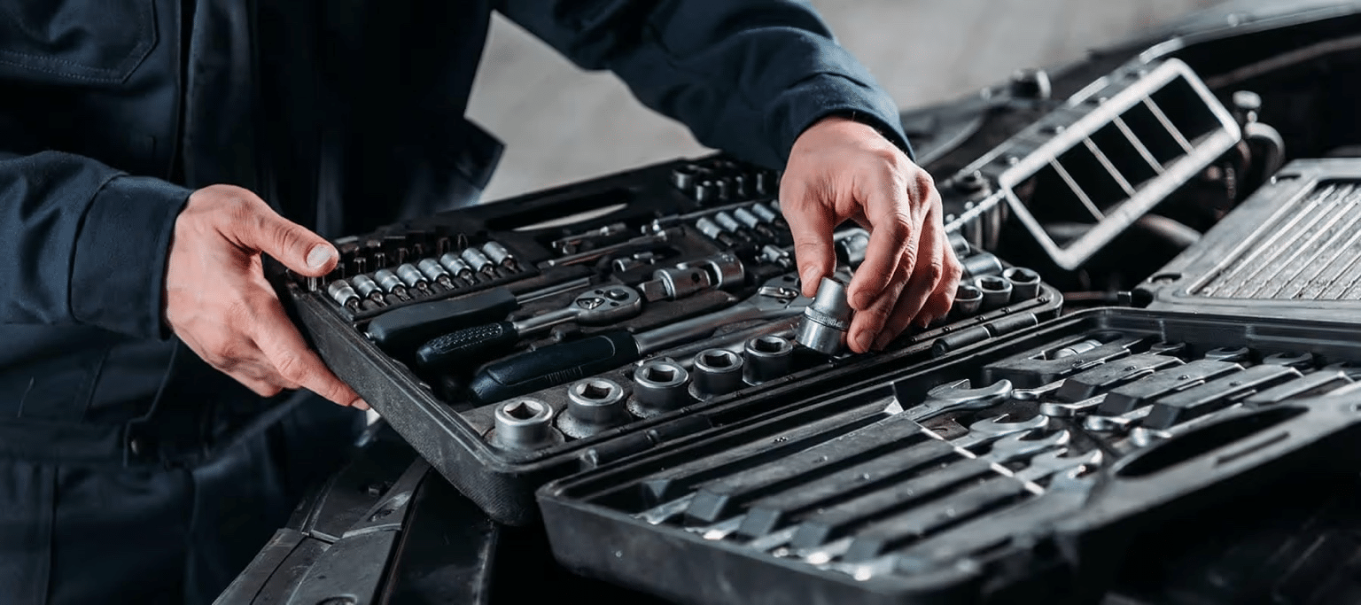 Mechanic organizing a tool kit with sockets and wrenches near an open car hood.