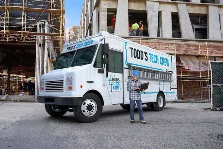Tech crew truck at construction site with worker in hard hat using a tablet.