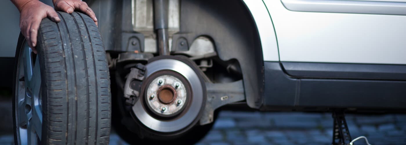 Person changing a car tire, showing the wheel removed and exposed brake disc.