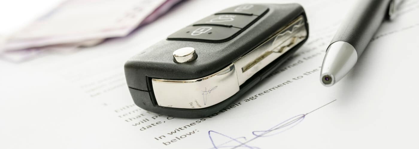 Car key and pen on signed document, indicating a completed car lease or purchase agreement.