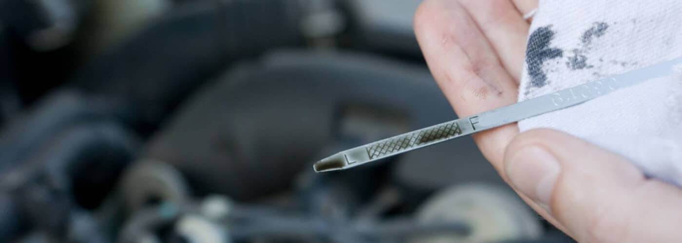 Hand holding a wiped car oil dipstick near an engine, showing low oil level markings.