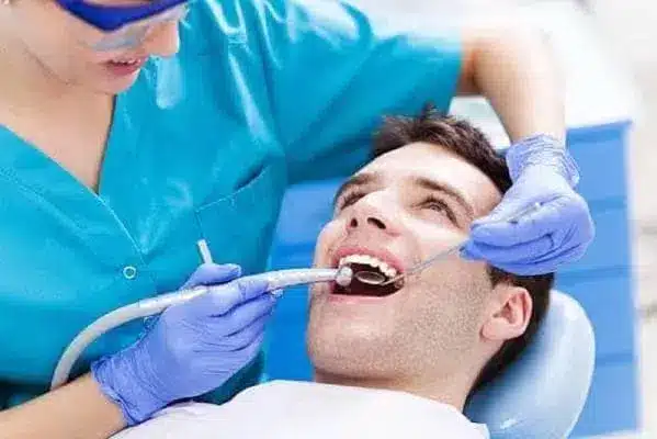 Dentist examining a smiling patient with dental tools in a clinic setting.
