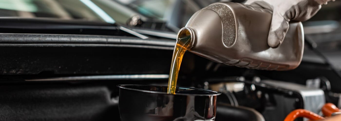 Pouring motor oil into a car engine using a plastic jug, showcasing vehicle maintenance.