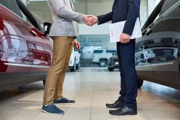Two people shaking hands in a car showroom, symbolizing a successful car sale.