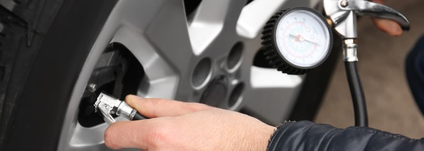 Hand using a pressure gauge to check tire pressure on a car wheel.