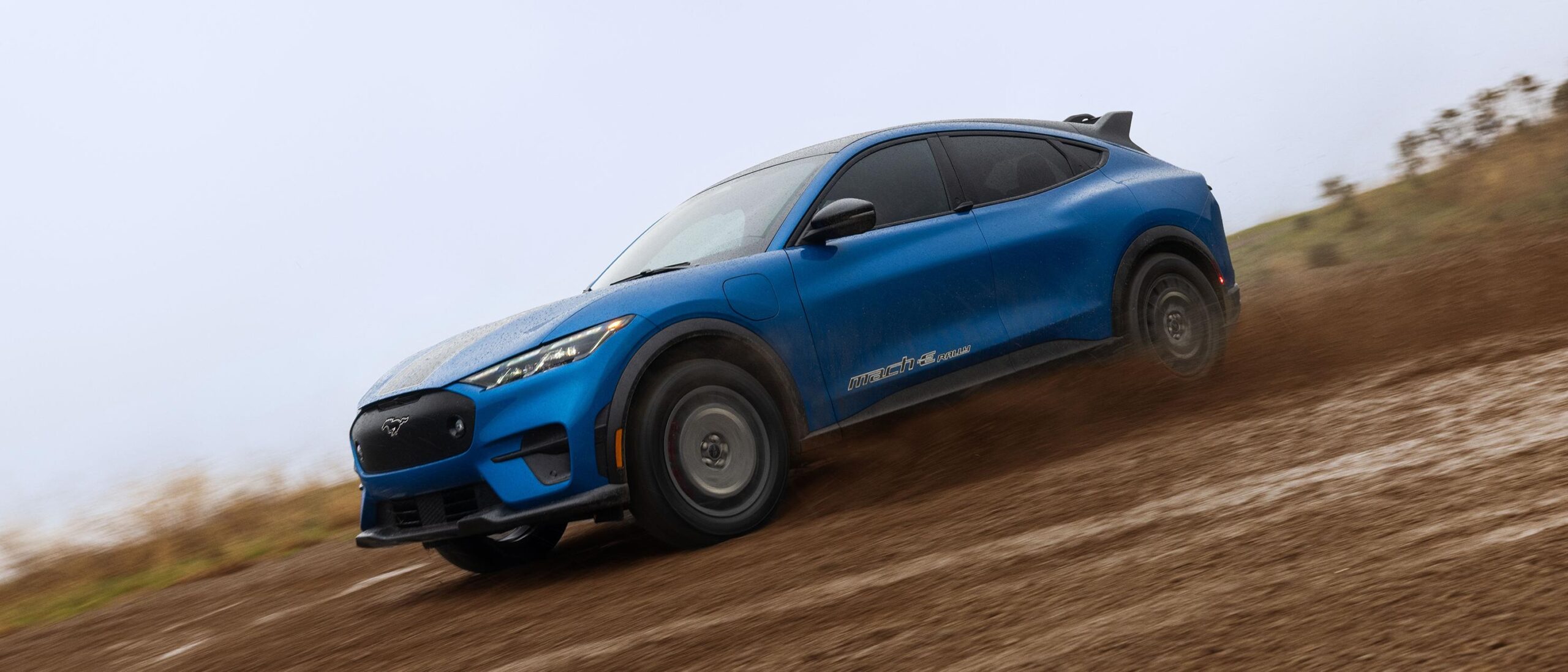 Blue electric SUV driving on a muddy path, showcasing off-road capability.