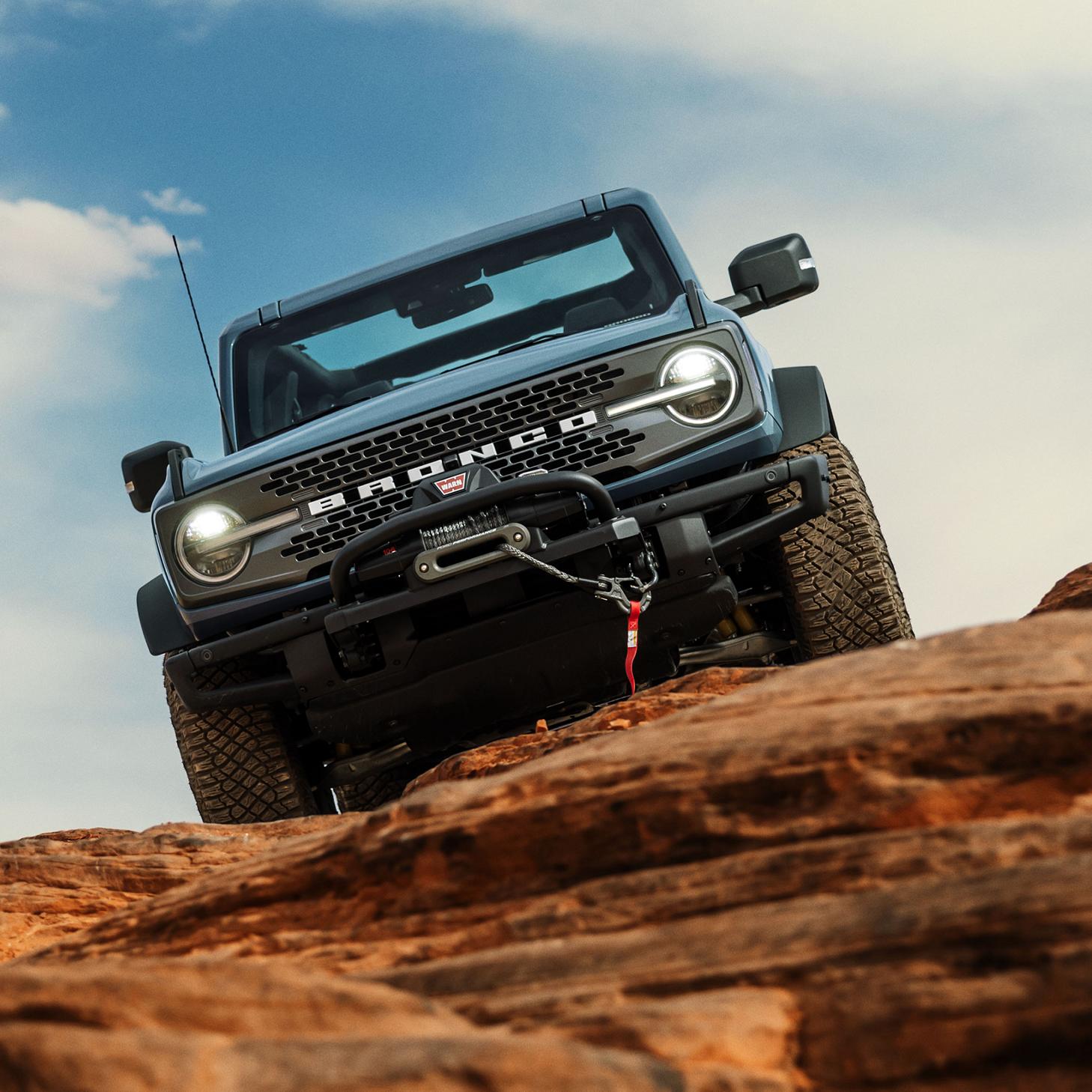 A Ford Bronco navigating rocky terrain under a clear blue sky, showcasing its off-road capabilities.